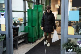 Eine Person mit Langstock verlässt einen Einkaufsladen.