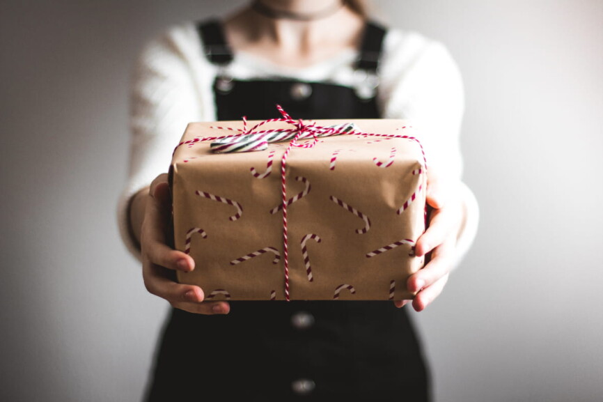 Person überreicht Geschenk, Symbolbild Weihnachtsshopping