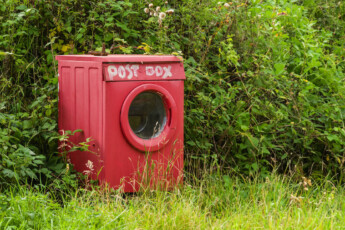 Eine rot bemalte Waschmaschine steht in der gr¸nen Landschaft und wurde zum Briefkasten umgebaut, auf einem Brett ist Postbox geschrieben. Isle of Mull, Schottland, Grossbritannien. Eine ungewˆhnliche Postbox *** A red painted washing machine stands in the green landscape and was converted into a mailbox, on a board is written Postbox Isle of Mull, Scotland, Great Britain An unusual mailbox