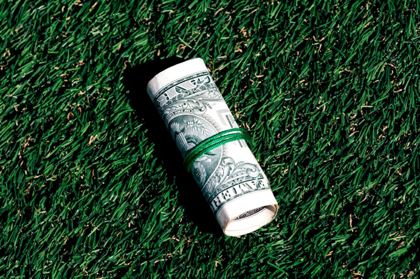 Closeup of rolled one dollar paper currency tied on green grass background with copy space
