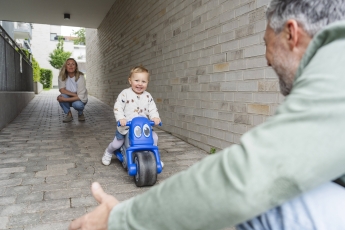 Child riding toy vehicle outdoors with parents enjoying quality time model released, Symbolfoto, IHF02425