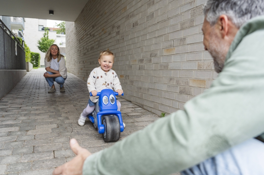 Child riding toy vehicle outdoors with parents enjoying quality time model released, Symbolfoto, IHF02425