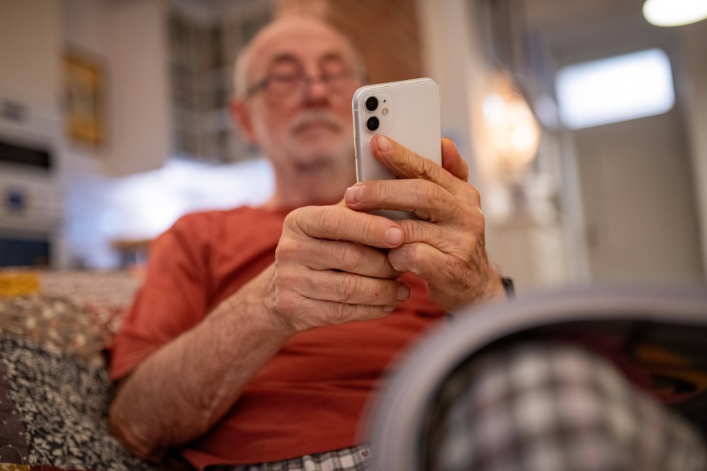 Elderly man holding and using a smartphone.