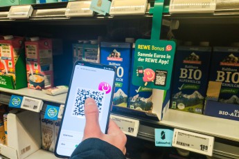 Bavaria, Germany – January 21, 2025: A customer holds his smartphone with the REWE Bonus app open in front of an adverti